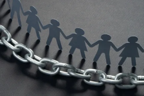 Paper cutout people holding hands above a metal chain symbolizing unity and strength together.