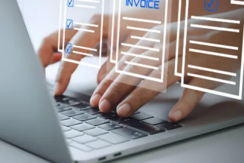 Person typing on laptop with digital invoices and documents floating above keyboard.