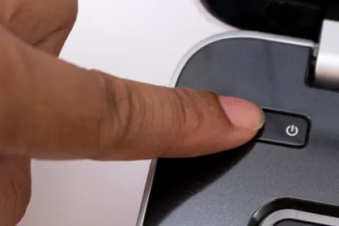 Finger pressing the power button on a laptop keyboard close-up with the esc key visible.