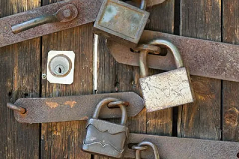 Rusty old padlocks securing weathered wooden doors with metal bars and a keyhole visible.