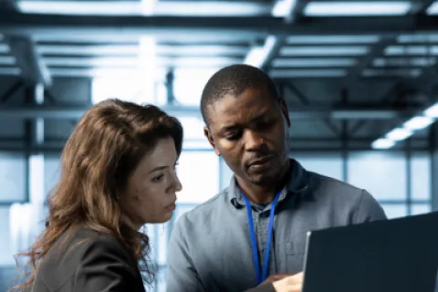 Two professionals reviewing information on a laptop in a modern office environment with natural light.