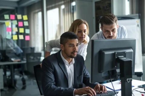 Three business professionals collaborating and working together at a computer in a modern office.