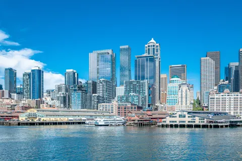 Clear blue sky over Seattle waterfront with modern skyscrapers and piers reflecting on water.