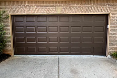 Brown paneled garage door on a brick house with concrete driveway and roof shingles.