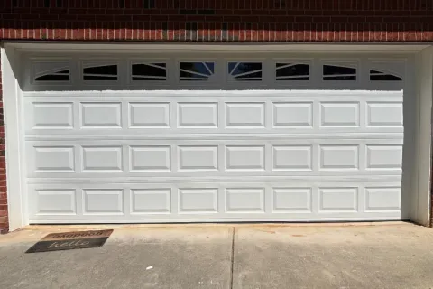 White paneled garage door with small windows at the top, set in a brick and siding house exterior.