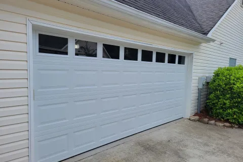 White garage door with small rectangular windows on a suburban house with beige siding and concrete driveway.