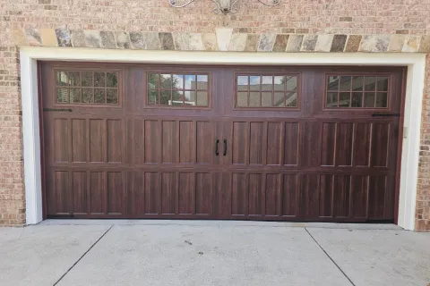Dark wood garage door with windows in a brick house and a decorative exterior light above.