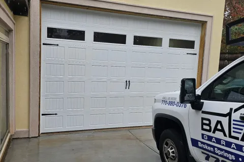 White residential garage door with decorative handles and windows beside a company truck on a wet driveway.