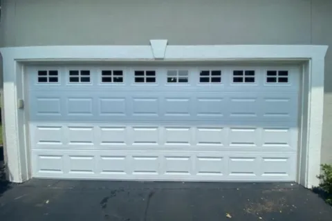 White residential garage door with decorative top windows and panel design on a driveway.