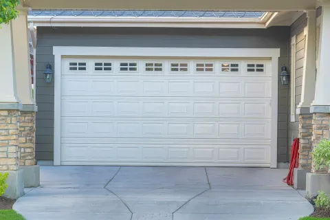 Front view of a modern white garage door with windows, stone pillars, and a concrete driveway.