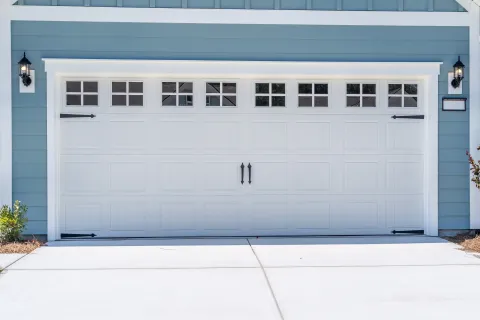 White paneled garage door with decorative windows and black hardware on a blue house exterior