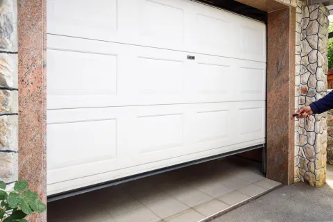 Person opening a white panel garage door surrounded by stone walls and granite frame.