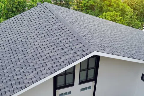 Modern house with newly installed grey asphalt shingle roof and white walls surrounded by greenery.