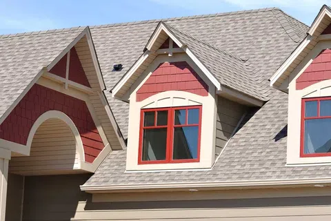 Close-up of a house roof with gray shingles and red framed dormer windows under a clear blue sky