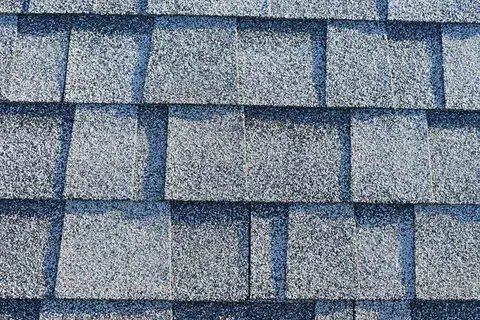 Close-up of gray asphalt roof shingles arranged in a staggered overlapping pattern under sunlight.