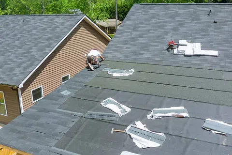 Roofer installing protective underlayment on a residential roof with tools and roofing materials laid out