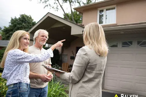 Older couple talking with a real estate agent outside their suburban home near the garage and garden
