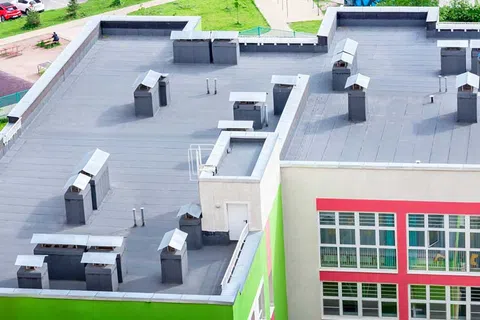 Aerial view of a building with a flat gray roof featuring multiple vents and colorful green and red exterior walls.