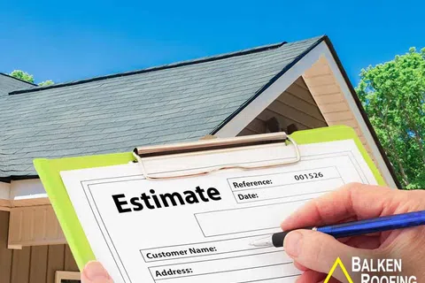Hand holding pen filling out a roofing estimate form with house and blue sky in the background.