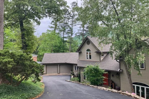 House with tan siding, red front door, double garage, and mature trees along a curved asphalt driveway.