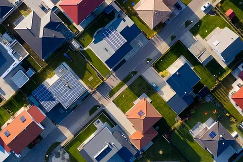 Aerial view of a suburban neighborhood with houses featuring solar panels and red roofs on a sunny day