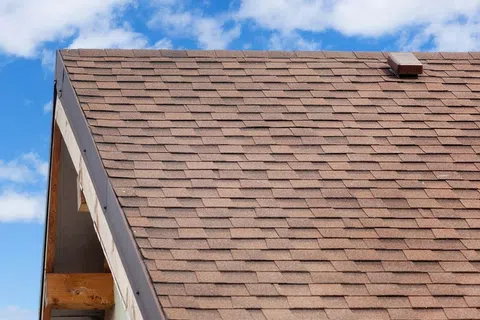 Close-up of a brown shingle roof under a blue sky with scattered clouds.