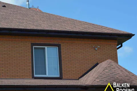 Brick house with brown shingle roof under clear blue sky, showcasing residential roofing design.