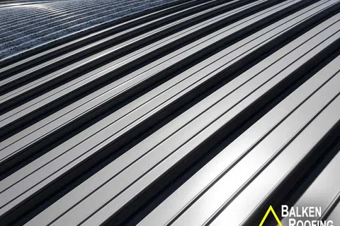 Close-up of silver metal roofing panels with reflective surface installed on a roof under clear sky.