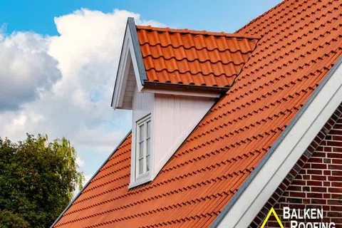 Orange tiled roof with a white dormer window on a house against a partly cloudy sky.