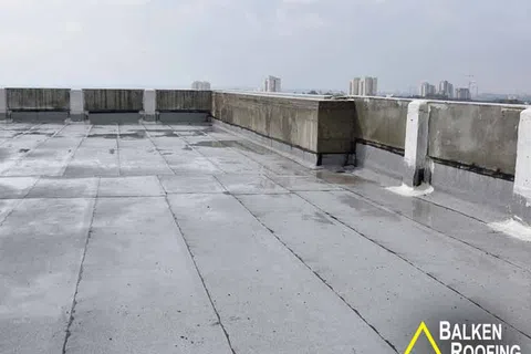 Flat rooftop with concrete barriers and waterproof roofing membrane on a cloudy day in an urban area.