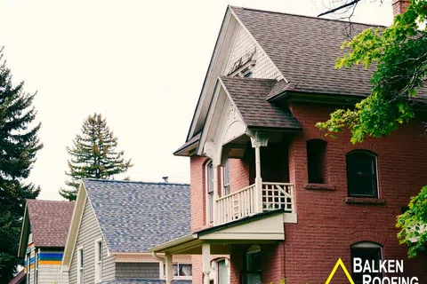 Traditional red brick house with gabled roofing and a wooden balcony surrounded by trees under clear sky