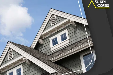 Close-up of modern house gable roof with gray shingles and white trim under blue sky