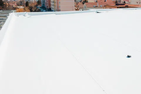 White flat roof membrane on building with urban landscape and residential buildings in the background