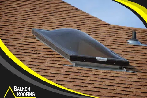 Curved skylight installed on a brown shingle roof with clear blue sky in the background