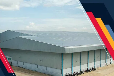 Large industrial warehouse building with motorcycles parked outside under a blue sky with clouds.