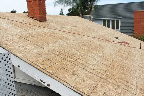 New plywood roof decking installed on a house with grid lines marked for shingle placement under a chimney.