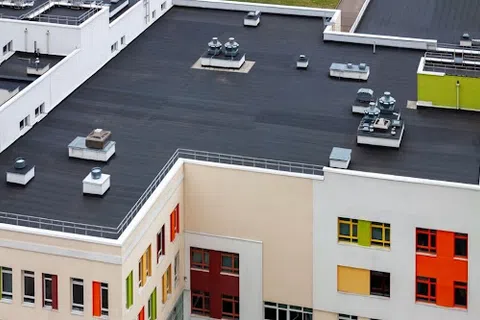 Top view of modern building rooftop with black flat roof and colorful window frames on beige walls.