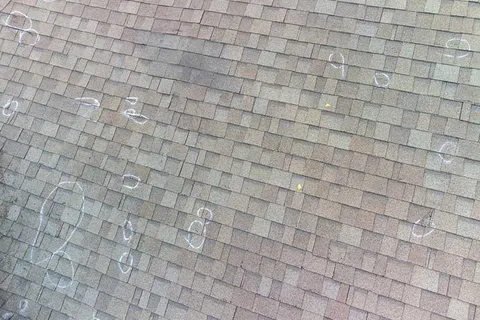 Asphalt shingle roof with multiple chalk circles marking damaged or impacted areas for repair.