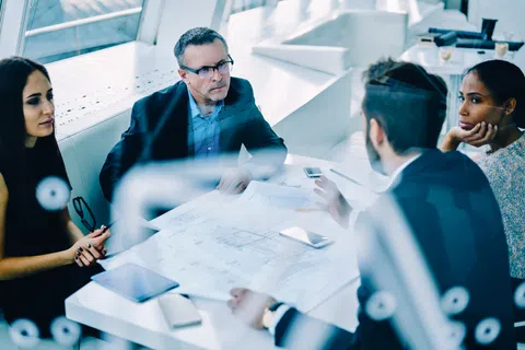 Four diverse business professionals engaged in a meeting around a table with documents and digital devices