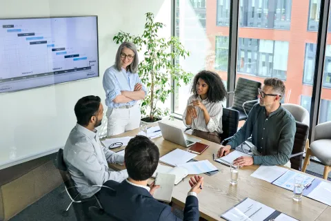 Team of five diverse professionals discussing project timeline on screen in modern office meeting room