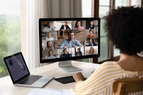 Person attending a virtual meeting with diverse colleagues on a desktop computer in a bright home office.