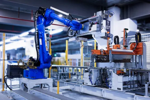 Industrial blue robotic arm operating machinery in a modern automated factory setting with metal components.