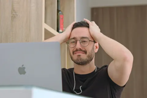 Man wearing glasses looking frustrated while using a slow and lagging laptop at a desk thanks to company downtime.