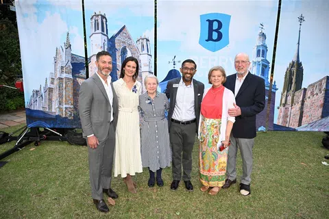 Group of six people posing outdoors on grass in front of large Berry College banners featuring campus buildings.