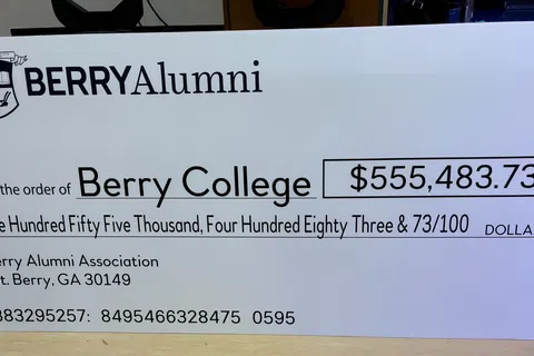 Giant check from Berry Alumni Association to Berry College for $555,483.73 donation displayed on table.