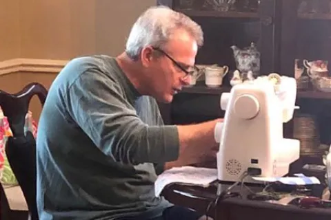 Berry alumnus Danny Price leans over sewing kit while making face masks