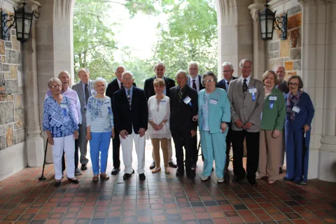 Group of elderly men and women posing together in an archway with name tags and ribbons