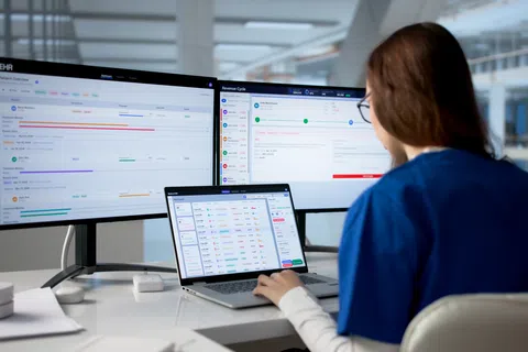 Healthcare professional using multi-screen electronic health record software in modern office setting.