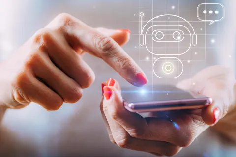 Person using smartphone with chatbot icon floating above, representing AI interaction and messaging technology.