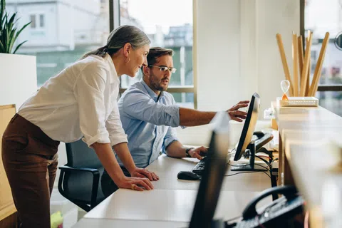 Man and woman collaborating at computer in a bright modern office setting focused on screen content.